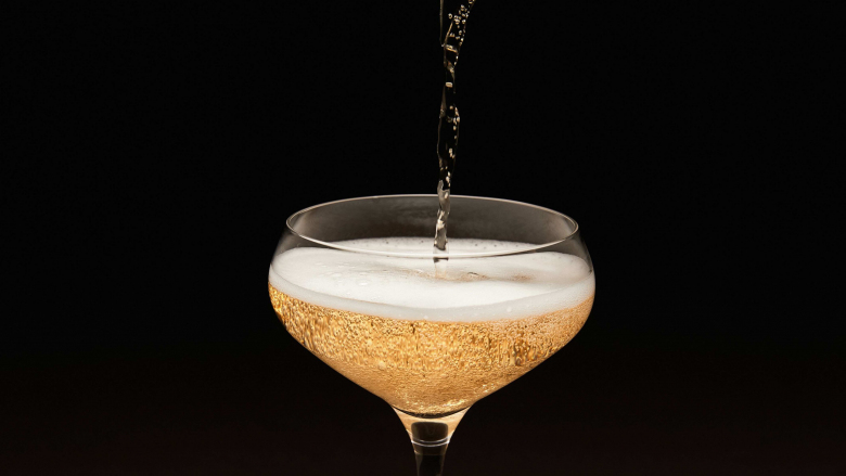Sparkling wine being poured into a coupe glass.